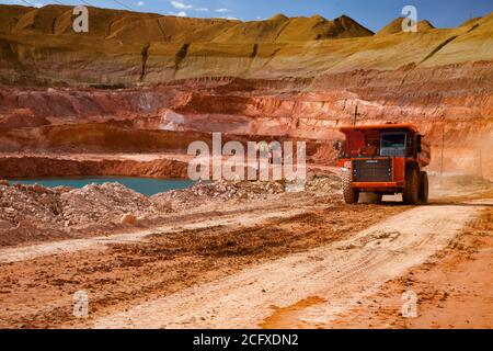 Estrazione e trasporto di minerali di alluminio. Estrazione in cava aperta. Dumper Hitachi arancione. Lago di cava blu. Cielo blu con nuvole di luce bianca. Foto Stock