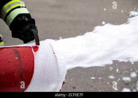 Fornitura di schiuma dal generatore di schiuma, schiuma antincendio vola dal generatore di schiuma, che mantiene il vigile del fuoco in abiti da combattimento Foto Stock