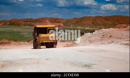 Estrazione e trasporto di minerali di alluminio. Miniera a taglio aperto di bauxite. Camion di cava gialla sulla strada bianca sul cielo blu con le nuvole nel giorno d'estate. Cumuli di scorie Foto Stock