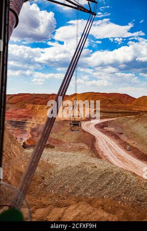 Bauxite creta aperto-taglio minerario. Cava di minerale di alluminio. Benna dell'escavatore a braccio mobile sul cavo del montante in funzione. Cielo blu, nuvole. Visualizzazione grandangolare Foto Stock