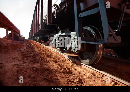 Bauxite creta aperto-taglio minerario. Terminal di carico e trasporto ferroviario. Primo piano delle ruote dei treni di carico e di un trasportatore (a sinistra) sulla parte posteriore in argilla bauxite rossa Foto Stock