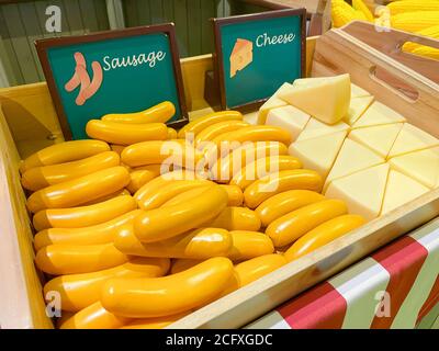 Salsiccia artificiale e formaggio in una scatola di legno come un disegno di mercato sullo sfondo di altre verdure e frutta, fuoco morbido. Foto Stock