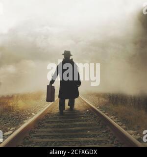 uomo misterioso cammina con la sua valigia sulle tracce verso una destinazione sconosciuta Foto Stock