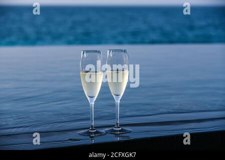 Un paio di flute di champagne sono allestiti sul bordo di una piscina infinity per una coppia da godere sul loro ponte privato in un resort di lusso nelle Maldive. Foto Stock