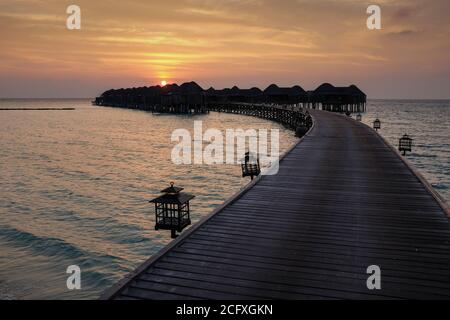Un molo curvo conduce al mare per raggiungere un gruppo di camere, o ville sull'acqua, in un resort di lusso nelle Maldive. Foto Stock