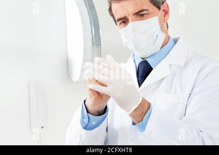 Il medico con una maschera per il viso indossa guanti sterili Foto Stock