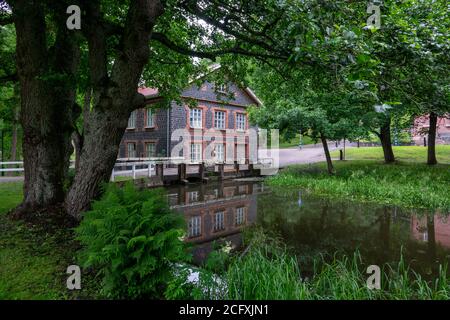 Fiskars villaggio e il suo mulino in estate. L'ex mulino di ferro lavori costruito di mattoni di scorie (costruito nel 1898). Alcuni alberi e un fiume, Finlandia. Foto Stock