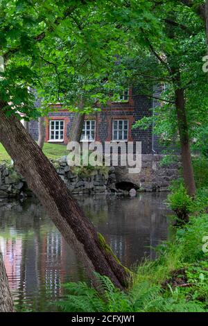 Fiskars villaggio e il suo mulino in estate. L'ex mulino di ferro lavori costruito di mattoni di scorie (costruito nel 1898). Alcuni alberi e un fiume, Finlandia. Foto Stock