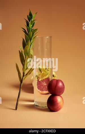 Una vita still di foglia che conduce su un bicchiere d'acqua con un fiore giallo e pesche su uno sfondo arancione che fa un look monocromatico. Foto Stock