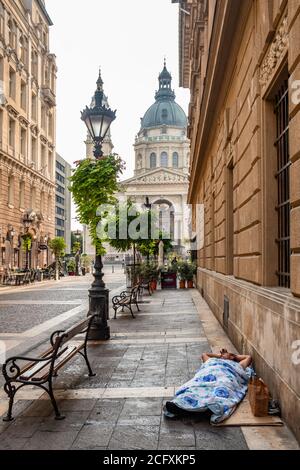 Un uomo senza dimora non identificato dorme sul marciapiede del via nel centro di Budapest Foto Stock