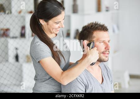 Donna taglia i capelli dell'uomo con il regolacapelli a casa Foto Stock