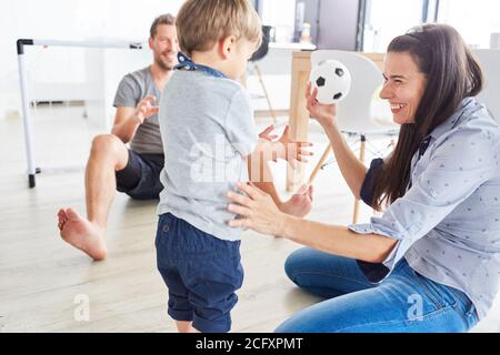 Felice madre che gioca a palla con suo figlio e con il padre sullo sfondo Foto Stock