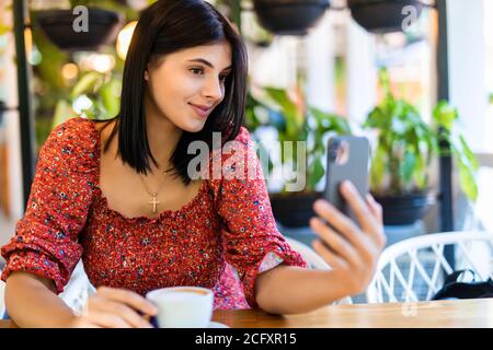 Giovane donna attraente in un caffè di strada che legge un testo messaggio dal suo telefono Foto Stock