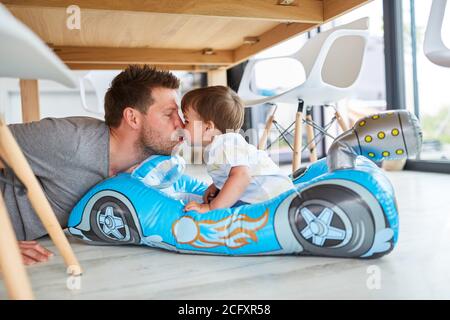 Padre dà al figlio un bacio nella vettura del bambino durante la riproduzione in soggiorno Foto Stock