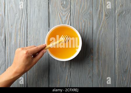 La mano femmina tiene il bilanciere in legno su sfondo di legno con il recipiente di miele Foto Stock