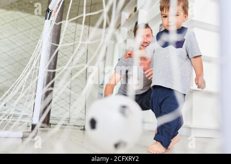 Il bambino che gioca a calcio segna un gol insieme al padre dentro il soggiorno Foto Stock
