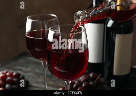 Il vino viene versato da una bottiglia in bicchiere su un tavolo di legno, da vicino Foto Stock