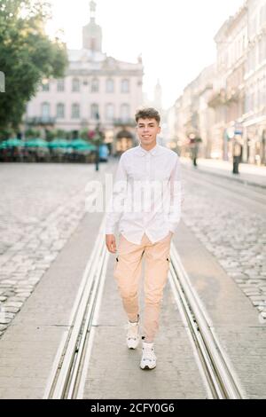 Giorno d'estate, passeggiata nel concetto di città. Vista frontale di un giovane ed elegante uomo caucasico vestito di camicia bianca e pantaloni beige, in piedi sulla strada della città Foto Stock