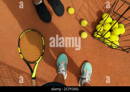 Le gambe di uomo e donna in sneakers su campo di argilla con palle da tennis e racchetta Foto Stock