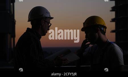 Lavoratori edili che hanno discussione al tramonto. Un fuma. Foto Stock