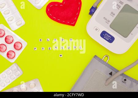 Il concetto di salute, cardiologia, pressione sanguigna. Parole DELLA PRESSIONE SANGUIGNA sui dadi. Monitor della pressione sanguigna, compresse e cuore tissutale su una ghiotta chiara Foto Stock