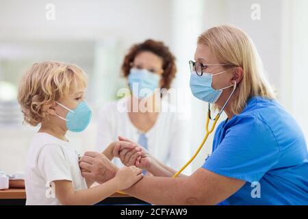 Medico pediatra che esamina il bambino malato nella maschera facciale. Ragazzo malato in clinica per test e screening. Trattamento domestico dei bambini del virus. Panda coronavirus Foto Stock