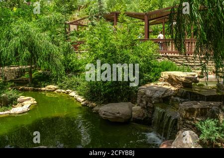 Teheran, Iran, luglio 07,2020: Piccola cascata con grandi massi di pietra e una recinzione di legno con gazebo per rilassarsi tra gli alberi nel 'mondo degli Uccelli' Pa Foto Stock