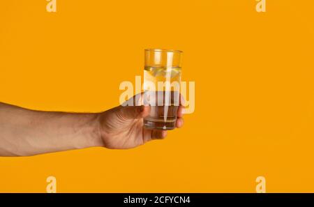 Giovane uomo che tiene un bicchiere di acqua potabile chiara su sfondo arancione, primo piano Foto Stock