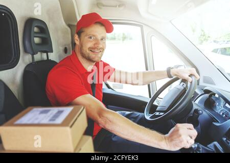 sorridente addetto al servizio di consegna in pulmino rosso uniforme e. consegna dei pacchetti Foto Stock
