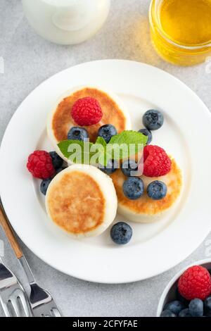 Syrniki, frittelle di formaggio di cottage con frutti di bosco e miele su un piatto. Colazione o dessert sani. Cheesecake Foto Stock
