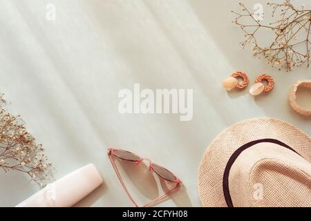 Accessori estivi femminili su sfondo blu. Occhiali da sole, cappello di paglia, orecchini, bracciale, bottiglia cosmetica e pianta gypsophila con ombre. Vista dall'alto, Foto Stock