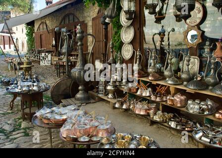 Una mostra di souvenir turchi tradizionali di bronzo e rame utensili da cucina artigianali e souvenir appesi alla parete sul pavimentazione in attesa Foto Stock