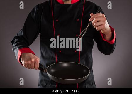 Primo piano dello chef che tiene la padella vuota e la forchetta. Concetto di preparazione degli alimenti, pronto per il posizionamento del prodotto. Foto Stock