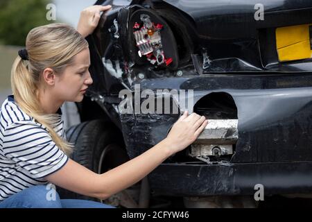 Infelice conducente femminile ispecting auto danneggiata dopo incidente Foto Stock