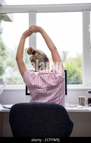 Vista posteriore di Donna che lavora da casa su computer in Home Office stretching alla scrivania Foto Stock