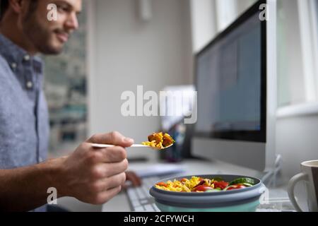 Lavoratore maschile in ufficio con un pranzo vegetariano sano alla scrivania Foto Stock