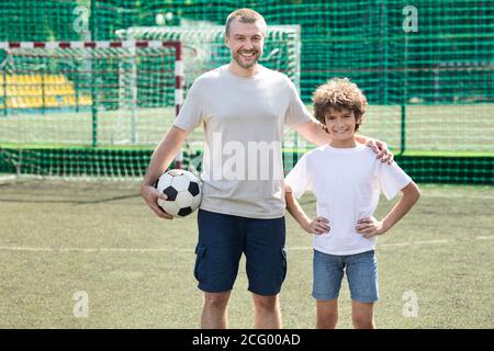 Uomo che tiene la palla in posa con il ragazzino sul campo da calcio Foto Stock