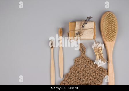 Set di zero rifiuti essenziali bagno su sfondo grigio - spazzolini da denti in bambù, boccioli di cotone, spazzola per il corpo in legno, panno per iuta e sapone organico, asciuga s Foto Stock