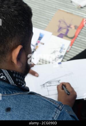 Un uomo con una giacca in denim che disegna un disegno di architettura in inchiostro. Foto Stock
