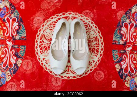 Vista dall'alto delle scarpe da sposa bianche collocate su un sfondo con motivo rosso Foto Stock