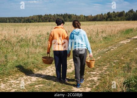 Madre e figlia hanno una passeggiata in famiglia in un campo, raccolta, famiglia con cestini di vimini raccogliere funghi o bacche, trascorrere il tempo all'aperto con yo Foto Stock