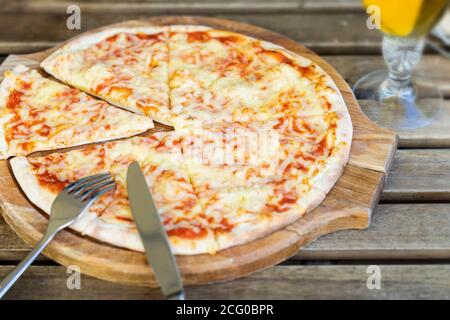 Pizza calda margarita appena sfornata su tavola di legno, primo piano. Posate, coltelli e forcelle, vista dall'alto. Cucina italiana in stile rustico Foto Stock