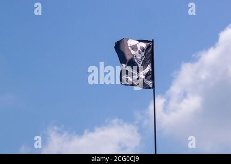 Bandiera pirata si sviluppa nel vento, cranio con ossa, Jolly Roger, il simbolo della rapina Foto Stock