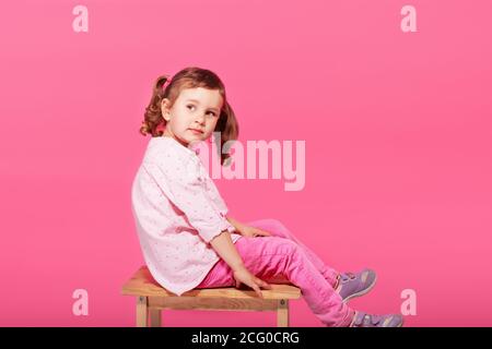 Bambino che gioca la scimmia. Bambina che indossa abiti rosa su sfondo rosa. Ragazza che mostra la lingua e divertirsi. Felice infanzia Foto Stock