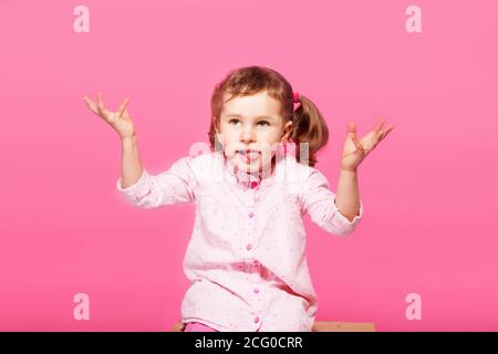 Bambino che gioca la scimmia. Bambina che indossa abiti rosa su sfondo rosa. Ragazza che mostra la lingua e divertirsi. Felice infanzia Foto Stock