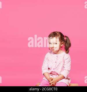 Bambino che gioca la scimmia. Bambina che indossa abiti rosa su sfondo rosa. Ragazza che mostra la lingua e divertirsi. Felice infanzia Foto Stock