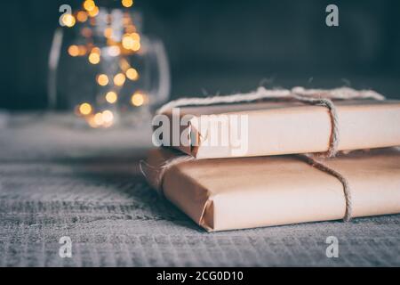 Due confezioni regalo o regalo avvolte in carta kraft su tavolo di legno e luci di vacanza sfocate sullo sfondo. Spazio di copia per il testo. Foto Stock