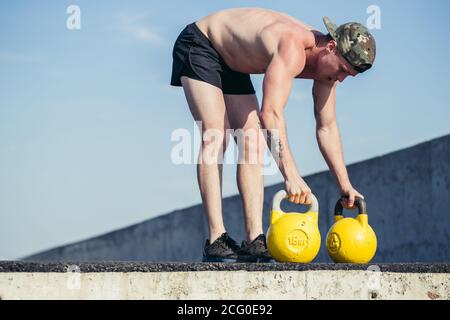 Ritratto in sezione bassa di un uomo irriconoscibile che solleva due pesanti campanacci con sforzo vigoroso durante l'allenamento in palestra Foto Stock