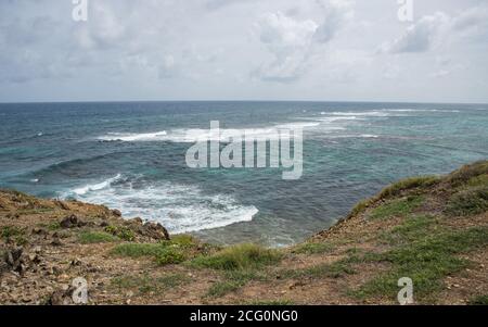 Vista elevata sulla scogliera costiera con le onde del Mar dei Caraibi che si ondeggia sotto un cielo nuvoloso a St. Croix, nelle Isole Vergini statunitensi Foto Stock