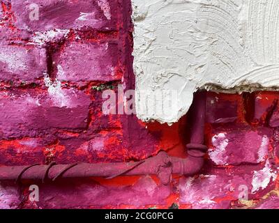 Vista su parete isolata in mattoni grezzi verniciata di colore bianco, rosa, viola e bianco con tubo dell'acqua (messa a fuoco su parete bianca a destra) Foto Stock